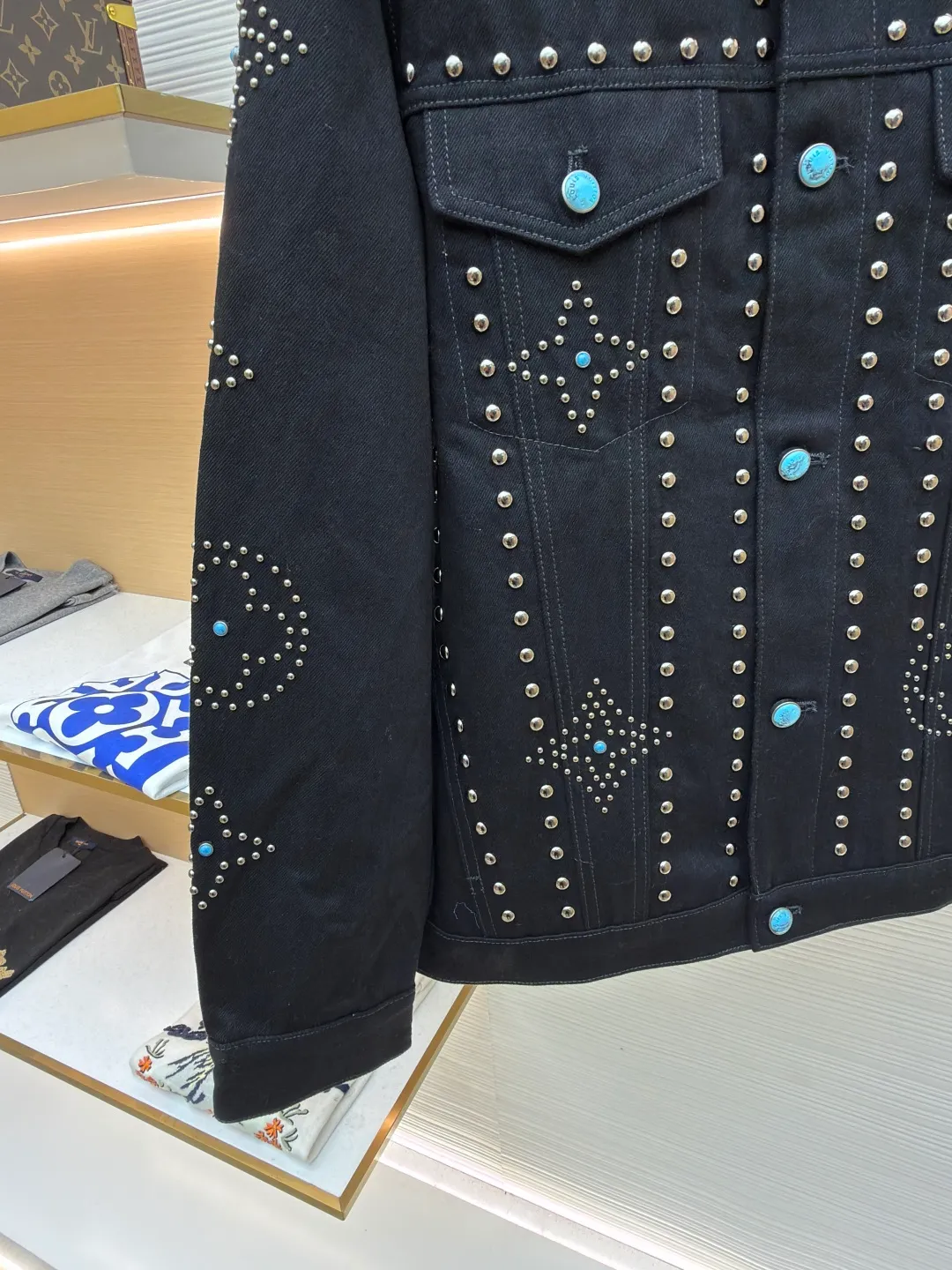 LOUIS VUITTON turquoise rivet denim jacket ●Original version: purchased and developed by 38979 ●Item number: 1682224-E30 ●Material: denim fabric ●Technology: hand-made rivet inlay ●Color: black ●Version: fitted version ●Weight: about 1550 grams ●Size: 46-48-50-52 ●Description: This black denim jacket is made of high-density twill denim fabric and has been treated with pre-washing water. It not only retains the crisp texture of the fabric, but also achieves a soft and skin-friendly wearing experience. The entire body of the garment is made of hand-made rivet inlay technology. The metal rivets are arranged at precise points to outline the outline of the brand's classic logo. Each rivet is manually hammered and fixed to ensure firmness and three-dimensionality. The placket and pockets are decorated with turquoise-textured resin buttons, which contrast with the metal rivets. The stitching on the collar, cuffs and hem adopts a double stitching process to enhance structural stability, while the edges are roughened to add a retro texture. The overall cut is a slightly loose Oversize version, combined with the three-dimensional tailoring process of the three-dimensional shoulder line, taking into account both styling and wearing comfort. Every detail is calibrated by hand, demonstrating the exquisite level of clothing making technology. The overall wiring is straight and delicate, the fabric is comfortable and soft, and the color is consistent without color difference. It can be matched with the same style to create a fashionable look and control various occasions. Customized accessories, complete with three standards, same style for men and women!